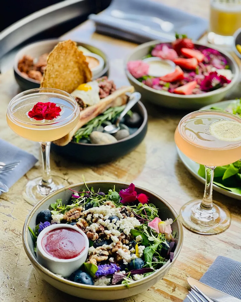 An overhead spread of brunch dishes — salads, tacos, and cocktails.
