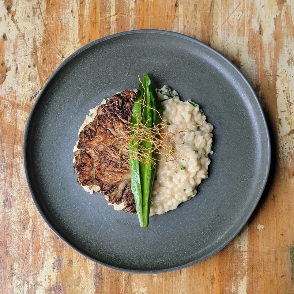 Crispy cabbage with risotto, plated overhead on a grey plate over a wood table.