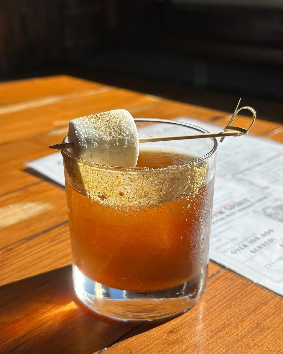 A smoked old fashioned cocktail with toasted marshmallow garnish in late afternoon light.