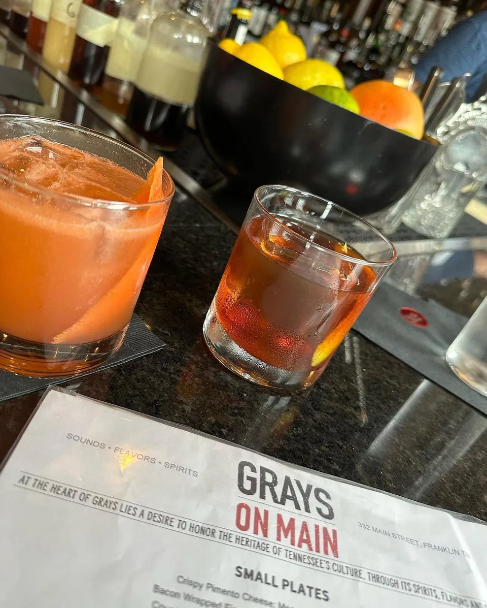 Two cocktails on the bar with a Grays on Main printed menu in the foreground.